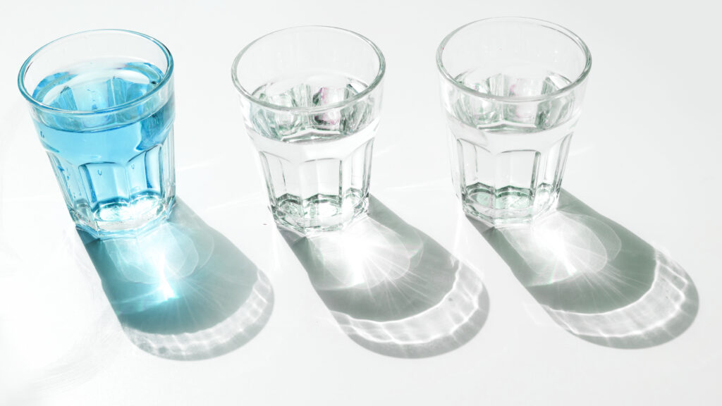 Tres vasos con agua de diferentes cantidades y tonos, iluminados por la luz natural, ideales para ilustrar conceptos sobre la cantidad recomendada de agua diaria según el peso corporal