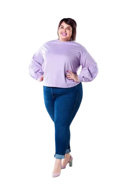 Mujer sonriente de talla grande con blusa lila de manga larga y jeans ajustados, posando con confianza y tacones rosados.